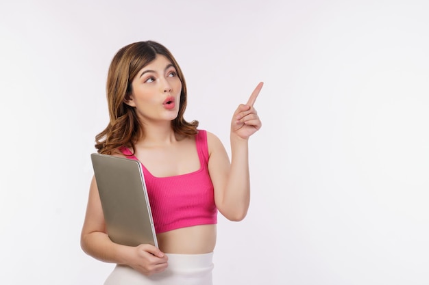 Portrait of young woman holding laptop computer and pointing finger aside isolated over white background