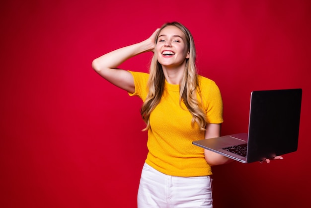 Portrait of young woman holding, working on laptop pc computer isolated on red wall.