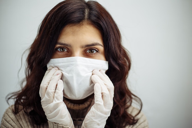 Portrait of a young woman holds hands on her head and has to stay home during quarantine due to coronavirus pandemia. Beautiful girl wearing medical mask and gloves. Covid-19 epidemia concept.