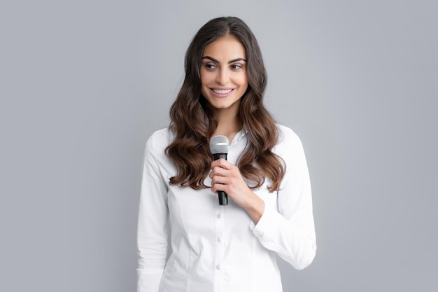 Portrait of young woman journalist in casual shirt holding microphone asking questions discussing problems interviewing Isolated on gray background