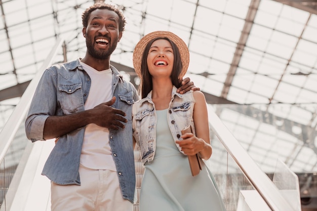 Portrait of young woman and man laughing together standing on escalator in shopping mall