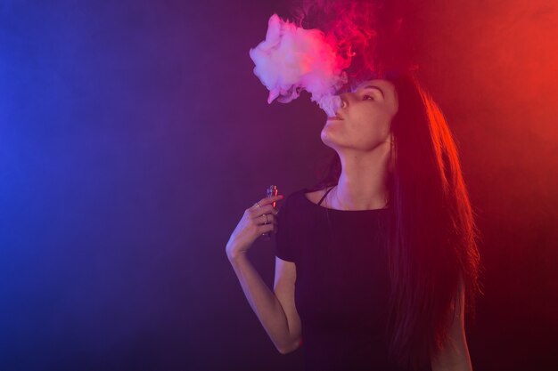 Portrait of young woman in neon red and blue smoke with vape or ecigarettes.