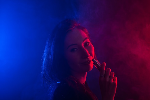 Portrait of young woman in neon red and blue smoke with vape or ecigarettes.