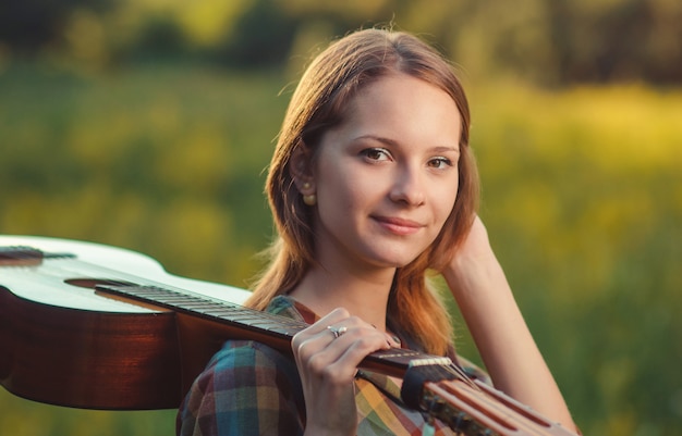 Portrait of a young woman in plaid shirt with a acoustic wooden guitar on shoulder