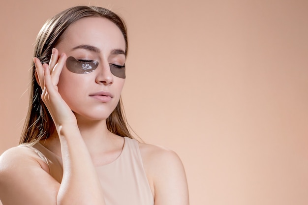 Portrait of young woman posing with applied black beauty patches under eyes over beige background