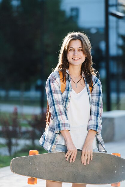 Portrait of a young woman posing with a skateboard in a park in the morning