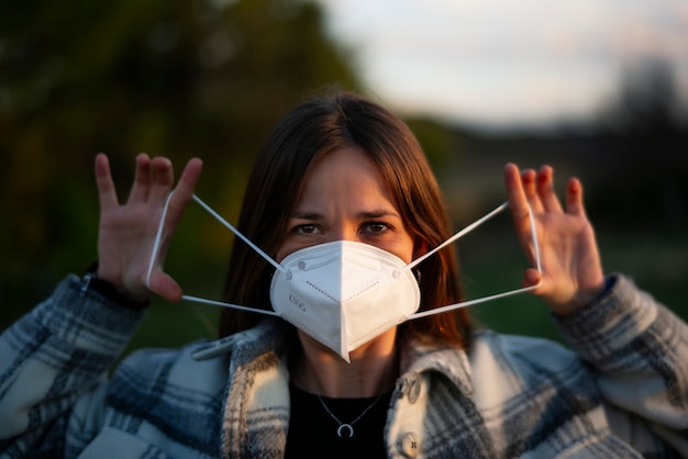 Portrait of young woman putting on protective mask outdoors