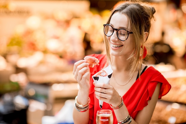 Portrait of a young woman in red dress eating jamon traditional spanish dry-cured ham sitting at the Barcelona food market