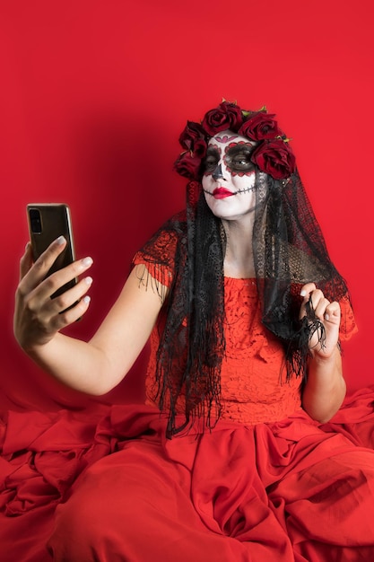 Portrait of a young woman in a red dress and traditional sugar skull makeup for the celebration of Dia de los Muertos the Day of the Dead