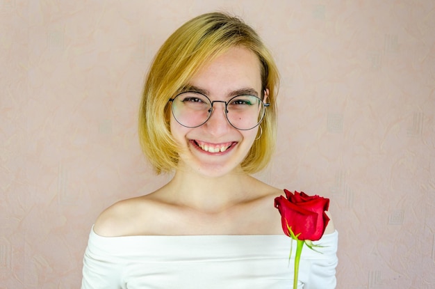 Portrait of young woman in round glasses with short blond ones holding red rose Sincere smile