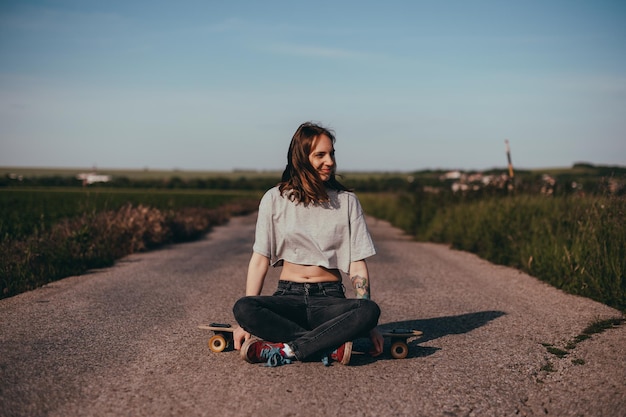 Portrait of a young woman sitting in the middle of the road alone on a longboard