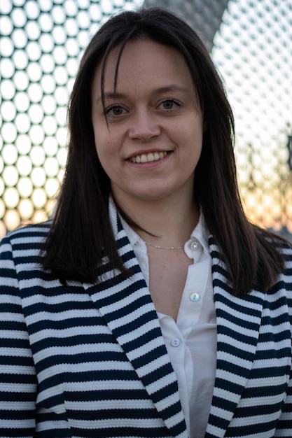 Portrait of a young woman smiling and looking at camera against a chain link fence outdoors