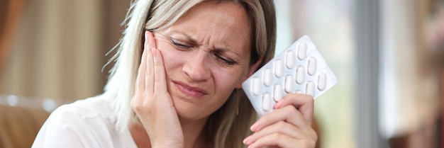 Portrait of young woman suffering from tooth pain and holding blister of pills toothache dental