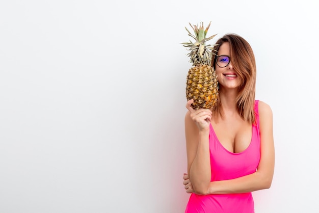 Portrait of young woman in swimsuit and eyeglasses with pineapple on white background. Summer season image concept