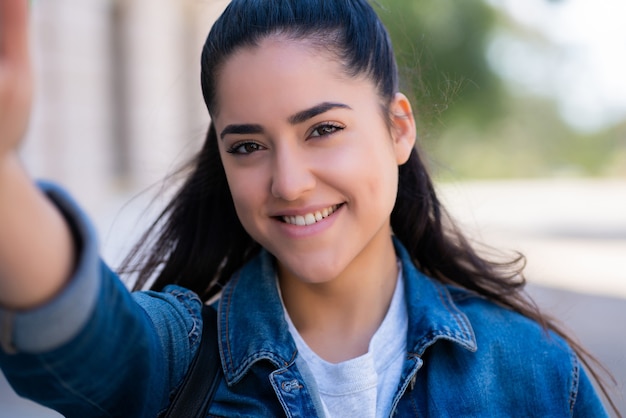 Portrait of young woman taking selfies while standing outdoors on the street.