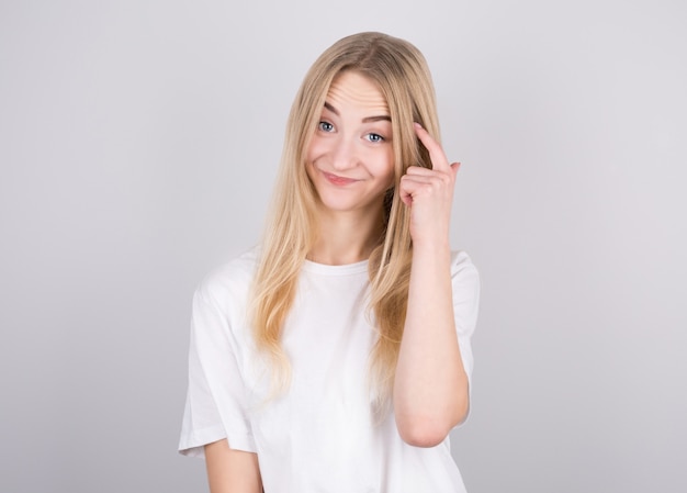 Portrait of young woman thinking with her finger to her head isolated over grey wall