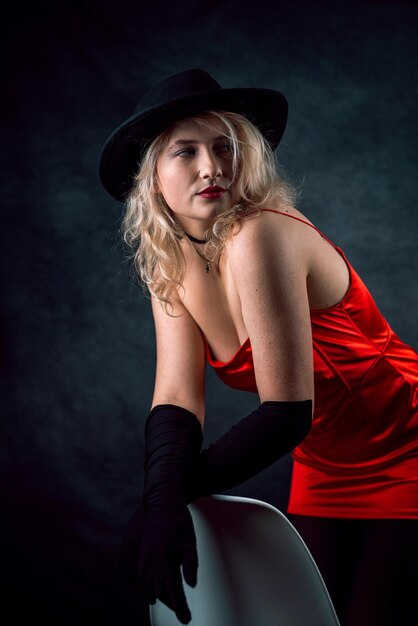 Portrait of young woman wear red dress and hat isolated on dark background