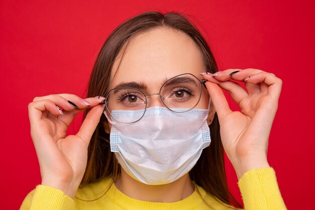 Portrait of a young woman wearing glasses and a protective mask on a red background