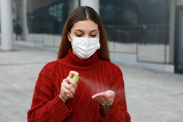 Portrait of young woman wearing protective medical mask spraying alcohol sanitizer on her hands