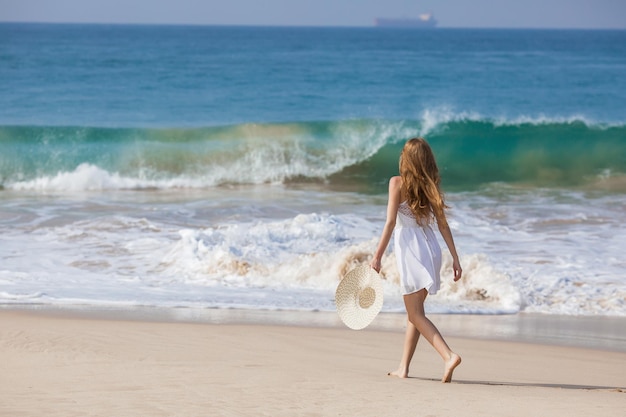 Portrait of young woman in white bikini on tropical beach looking at camera Beautiful latin girl in swimwear with copy space Summer vacation and tanning concept