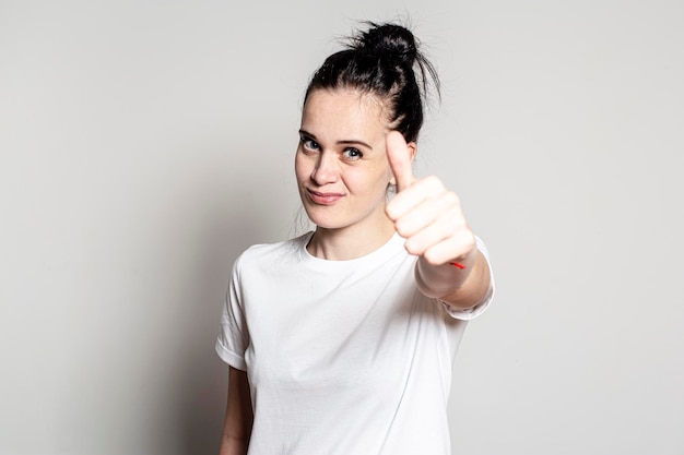 Portrait of a young woman who shows a thumb up gesture smiles slyly and looks at the camera