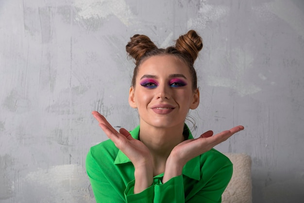 Portrait of young woman with bright makeup and bun hairstyle in green shirt Gray background