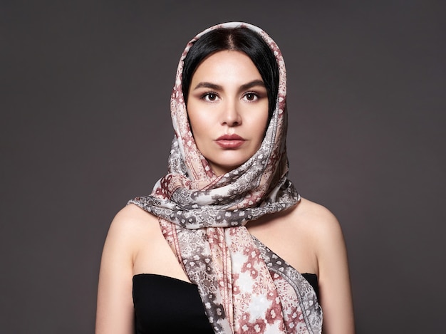 Portrait of a young woman with bright makeup and a fashionable scarf. Gray background. Beauty, fashion.