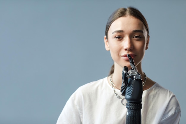 Portrait of young woman with disability having prosthetic arm looking at camera against blue backgro