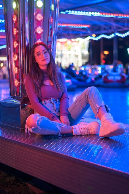 Portrait of a young woman with eyeglasses illuminated by the lights of a fairground