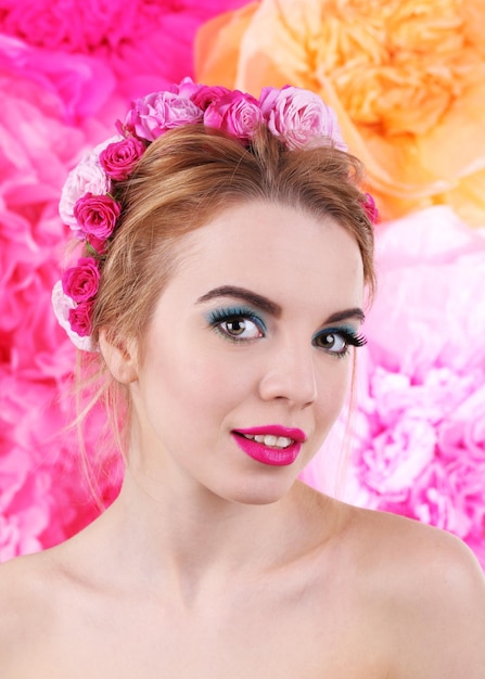 Portrait of young woman with flowers in hair on bright pink background