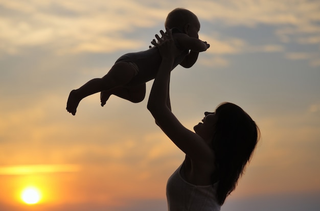 Portrait of young woman with little baby as silhouette by the water 