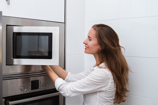 portrait of a young woman with long hair cooking in a microwave oven opening the door and taking out food