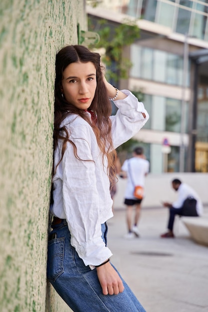 Portrait of a young woman with long hair looking at the camera on a wall in green tones