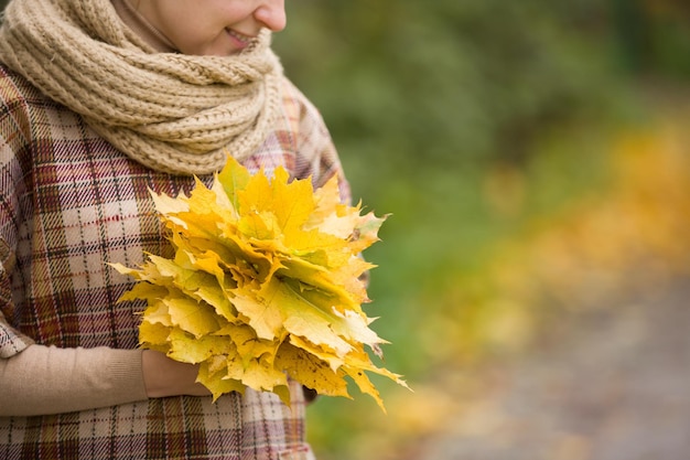 Portrait of young woman with maple leaves on autumn sunset background. Lifestyle and autumn concept