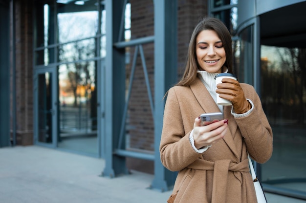 Portrait of young woman with paper cup of coffee and smartphone in the city