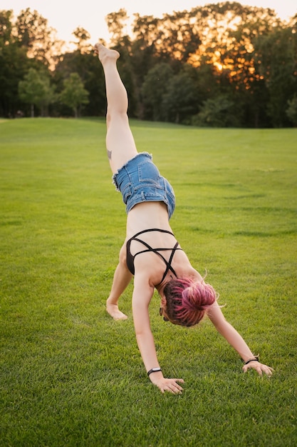 Portrait of young woman with pink dreadlocks doing yoga outdoors in the park on sunset. Freedom and health concept