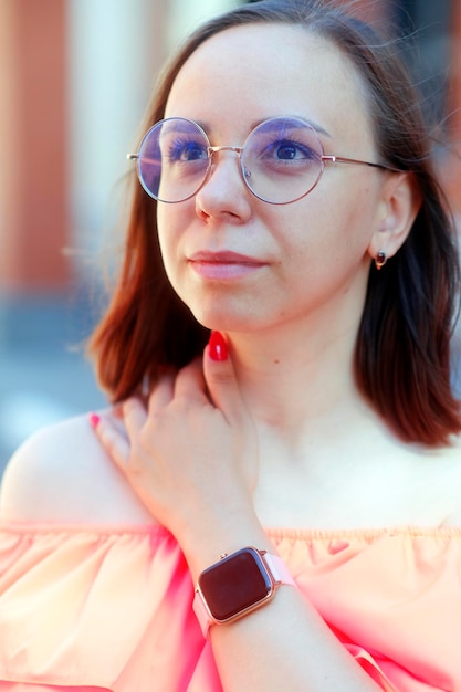 Portrait of young woman with short hair in glasses looking away standing on city street in warm windy weather