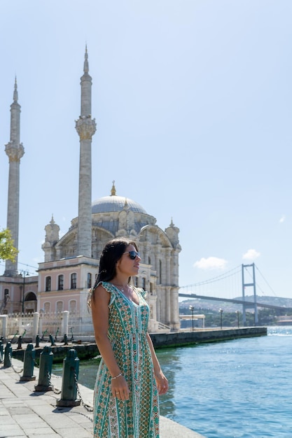 Portrait of a young woman with sunglasses posing in front of the ortakoy mosque and the famous bridge in istanbul