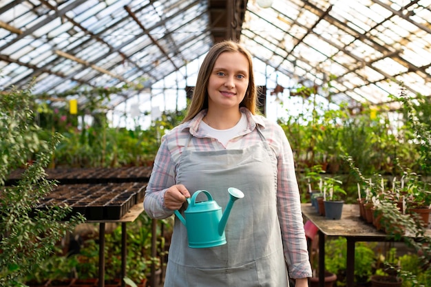 Portrait of a young woman working in a greenhouse she looks into the camera smiles and holds a