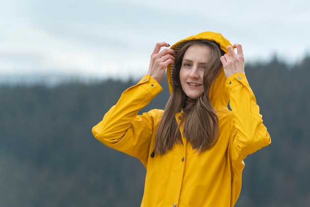 Portrait of young woman in yellow raincoat outside Girl on hike in autumn look at camera