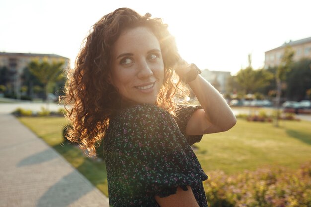 Portraits of a charming red-haired girl with freckles and a pretty face. The girl poses for the camera in the city center. She has a great mood and a sweet smile