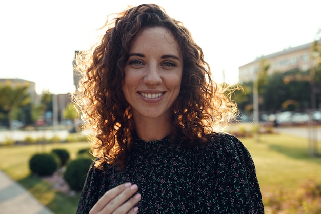 Portraits of a charming red-haired girl with freckles and a pretty face. The girl poses for the camera in the city center. She has a great mood and a sweet smile