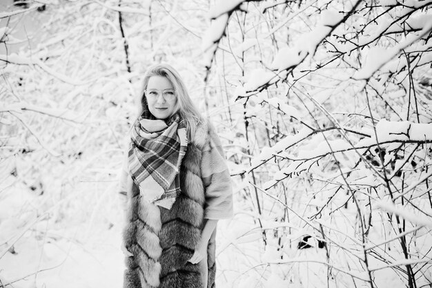 Portraiy of blonde girl in glasses, red fur coat and scarf at winter day.