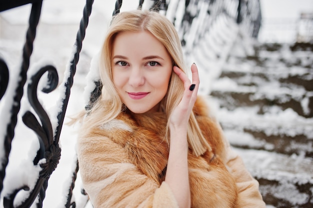 Portraiy of blonde girl in glasses, red fur coat and scarf at winter day.