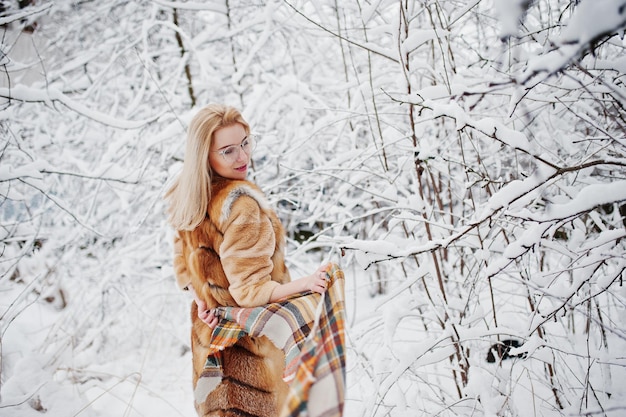 Portraiy of blonde girl in glasses red fur coat and scarf at winter day