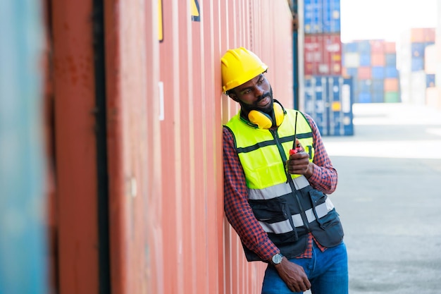 Portriat handsome male African American Industrial and factory Specialist Black man worker wearing yellow protective hard hat helmet working at container yard