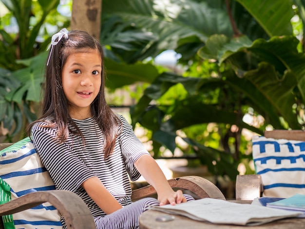 Portriat image of 8 years old Asian girl reading or doing homework at her backyardSchool kid in holiday in the garden