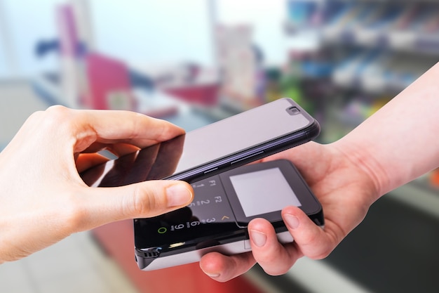 Pos terminals and smartphone. In the background is a supermarket checkout. Banking equipment. Acquiring. Acceptance of bank credit cards. Contactless payment.	
