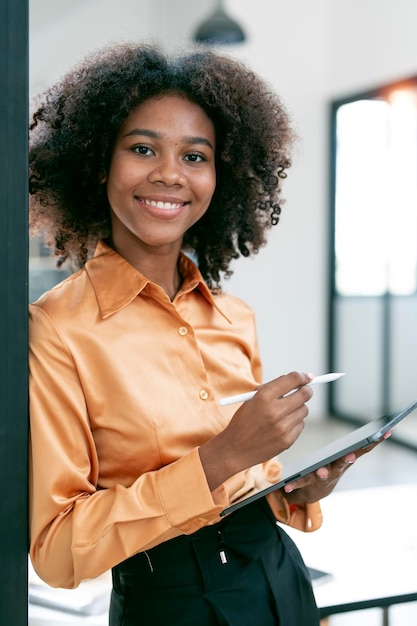 Positive african american business lady using digital tablet standing in office smiling to camera