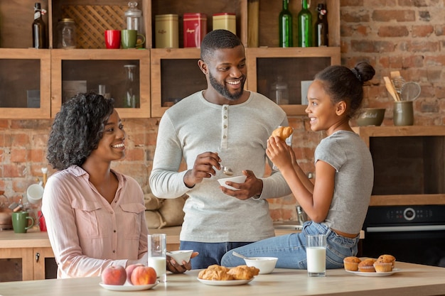 Positive african american family having breakfast in beautiful kitchen, talking while eating, free space